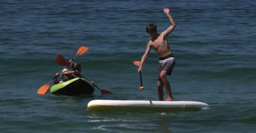 Man standing on a paddleboard next to a green kayak with two paddlers on the water
