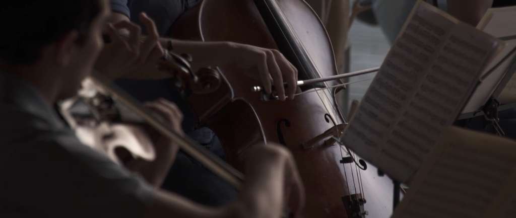Close view of hands playing a cello and violin beside sheet music