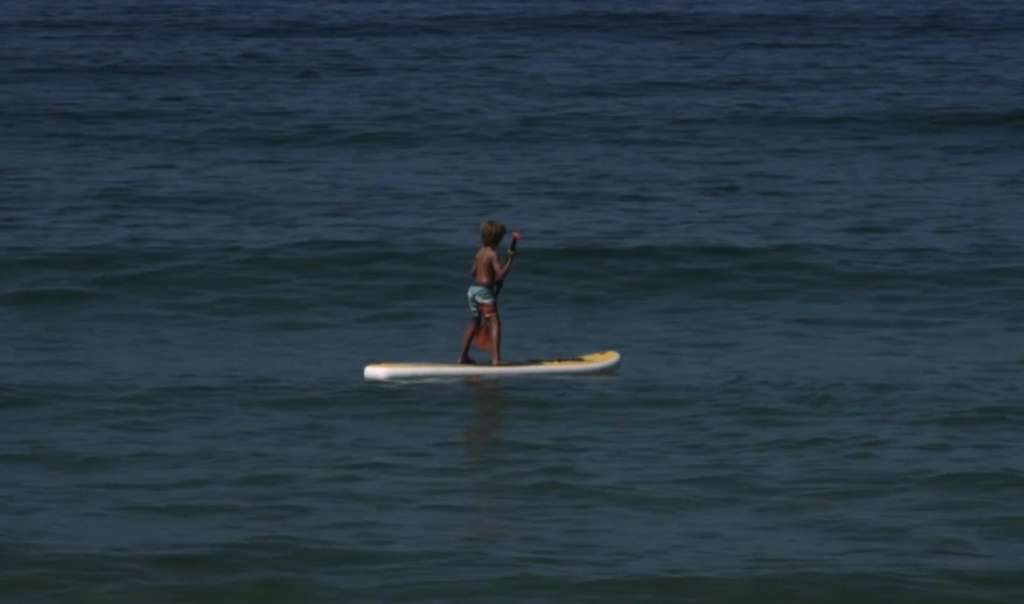 Child standing on a paddleboard on dark blue water
