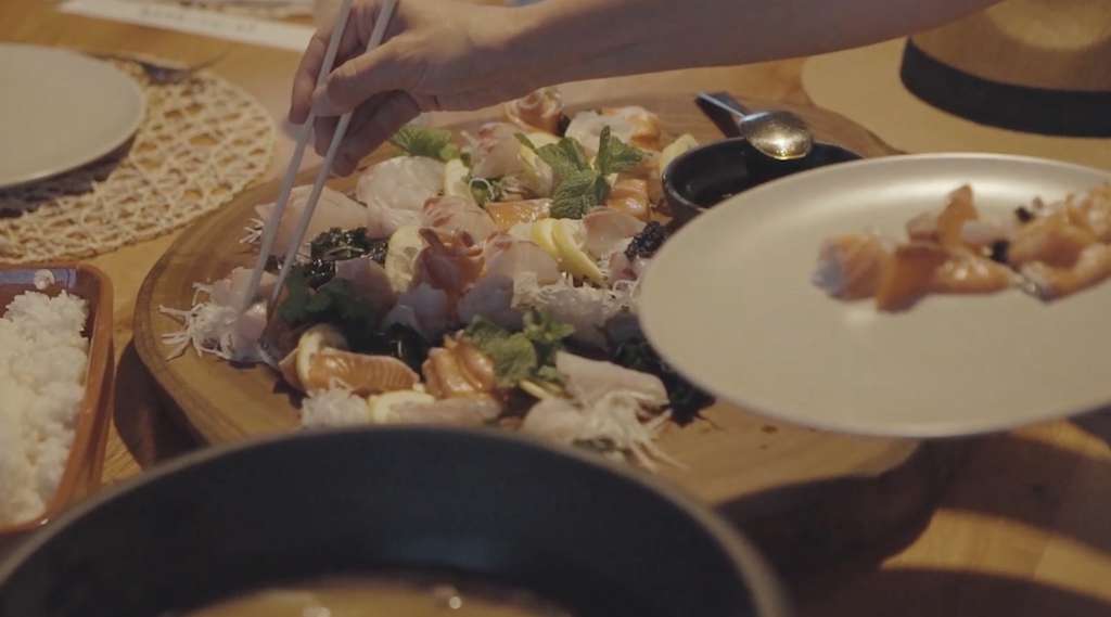Chopsticks picking sashimi from a wooden platter with lemon and herbs, rice nearby