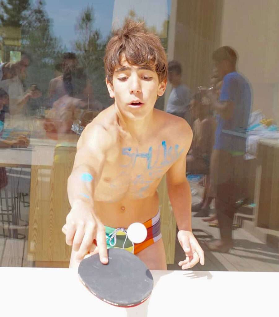 Shirtless boy about to hit a ping pong ball with a paddle