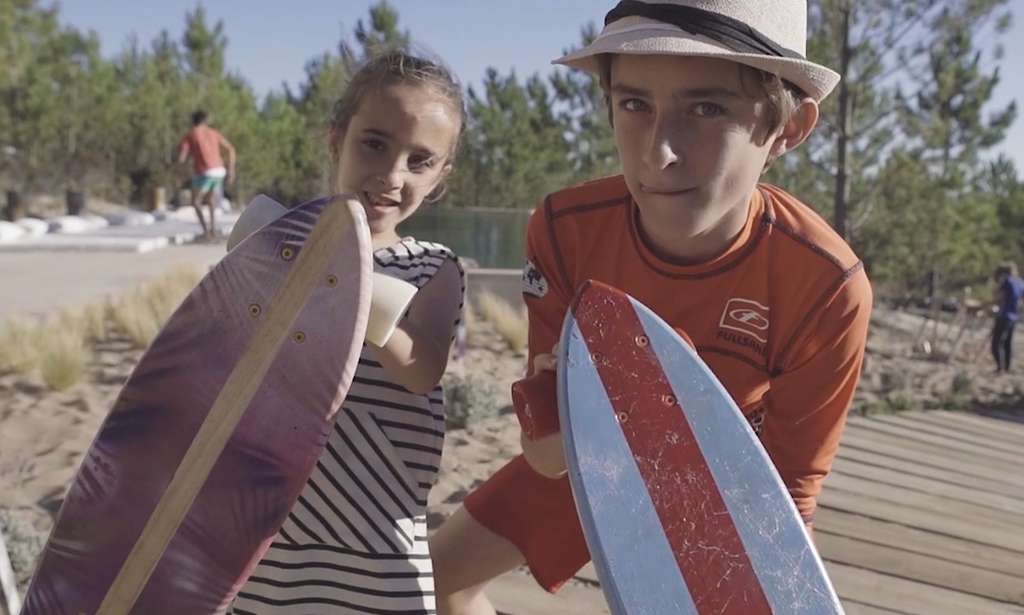 Girl and boy holding up two skateboards outdoors near sand and a pool