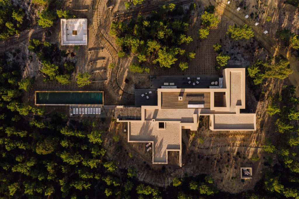 Aerial view of a sand-colored house with a long pool and deck among pine forest